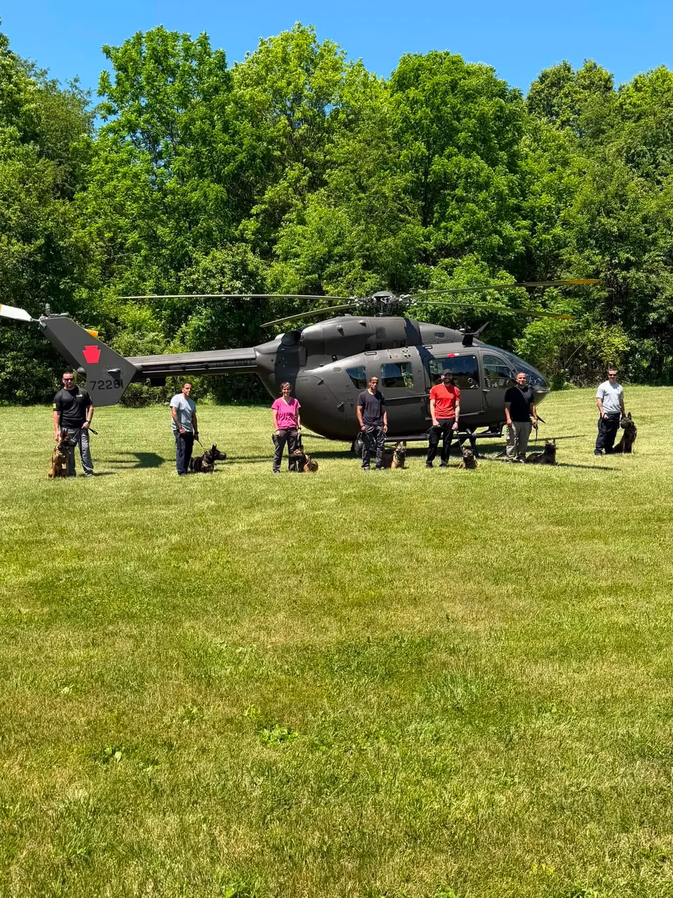 Seven K9 handlers with their dogs lined up in front of a helicopter during field training