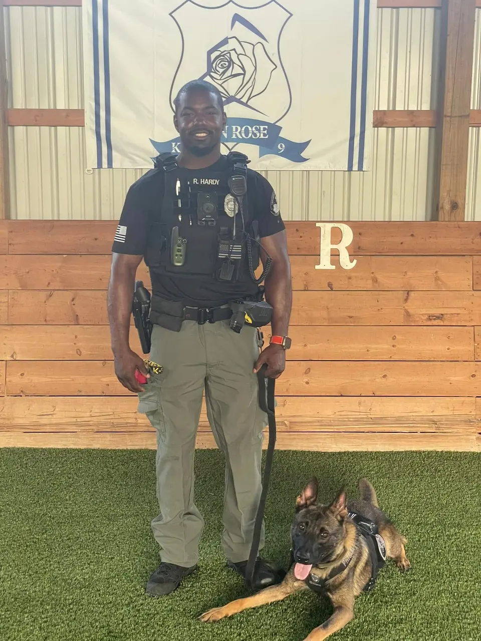 A uniformed K9 handler with a police dog in front of the Iron Rose K9 banner