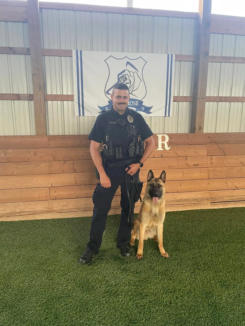 A police officer with a German Shepherd K9 in front of the Iron Rose K9 banner